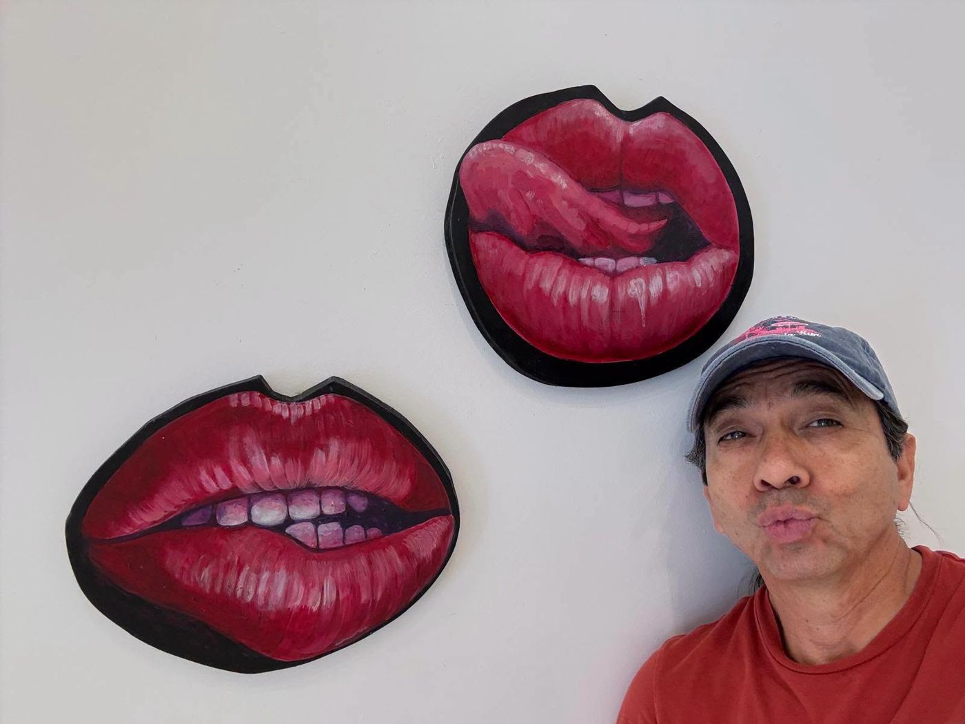 A visitor making a kiss face under two painted lips on the wall